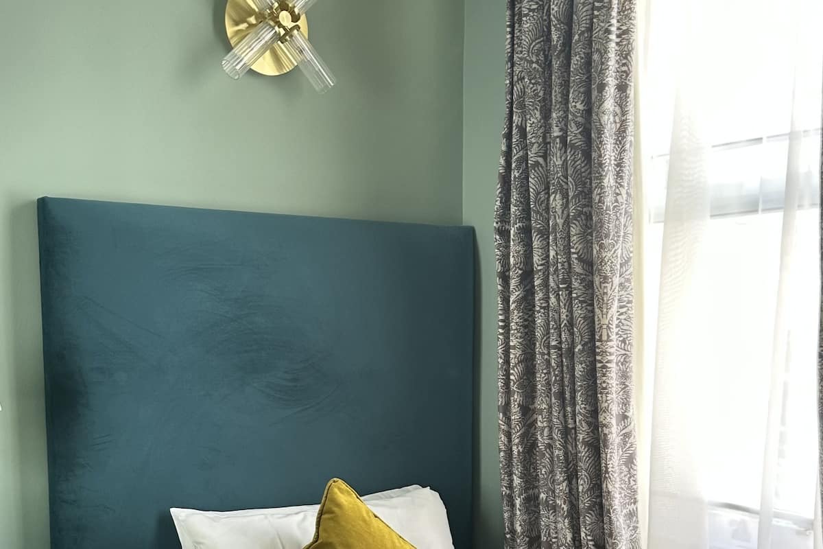 A hotel room with a bed, a bedside table, a wall clock, and a window with curtains.
