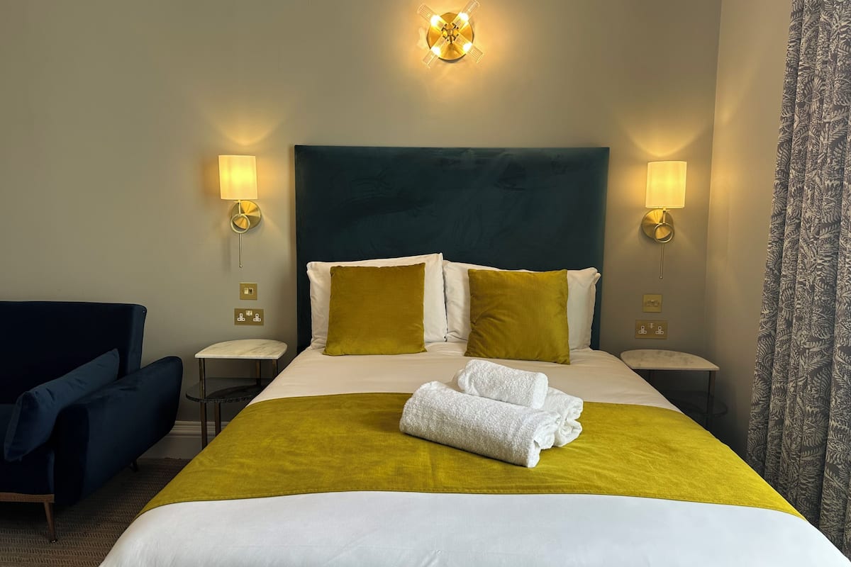 A hotel room with a large bed, two bedside tables, a chair, and a wall-mounted light fixture.
