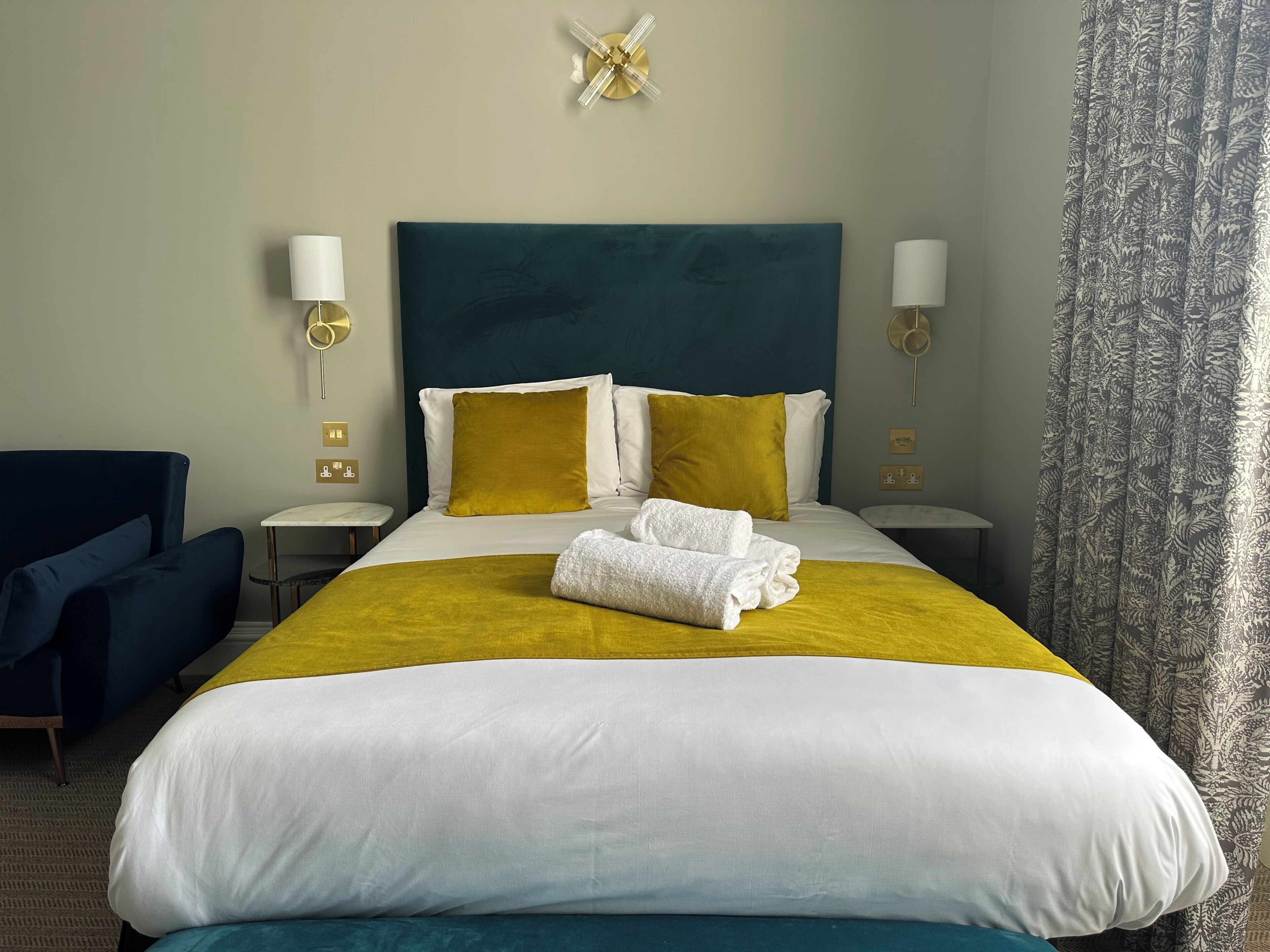 Une chambre d’hôtel avec un grand lit, deux tables de chevet, une chaise et une fenêtre avec des rideaux.