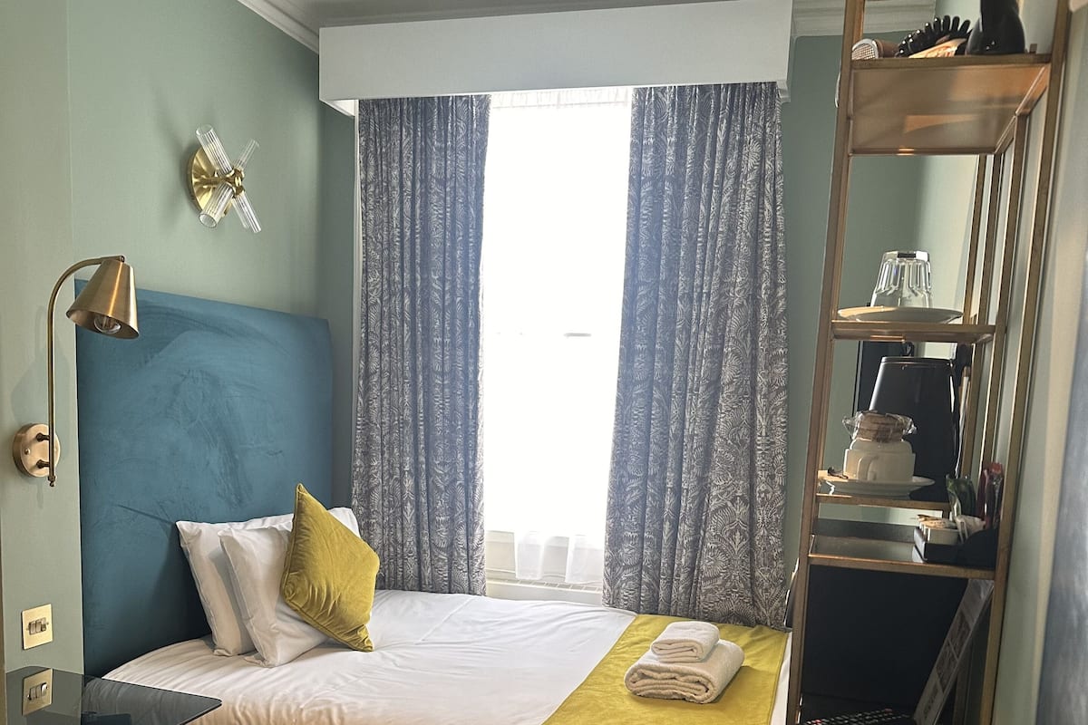 A hotel room with a bed, a desk, a chair, a mirror, and a window with curtains.