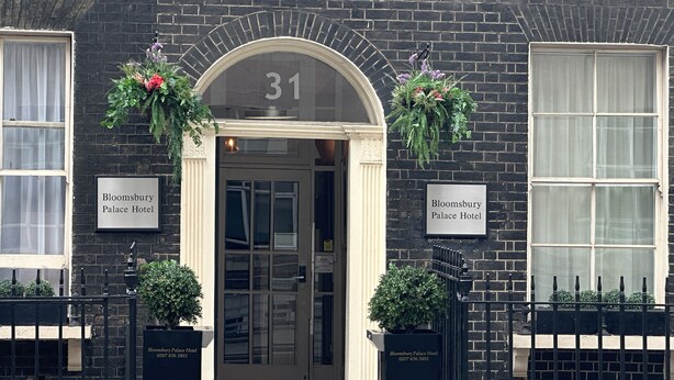 La entrada del Hotel Bloomsbury Palace, con un amplio arco en la puerta con el número 31, dos cestas de flores y una valla de metal negro.