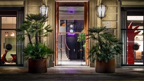 Ein Hotel Eingangsbereich mit einer Treppe zum Innenraum, Zimmerpflanzen und einem Parkroller vor der Tür.