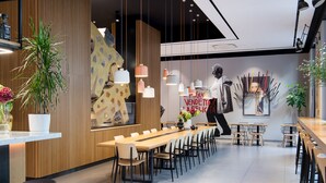 Ein modernes Restaurant-Interieur mit langen Gemeinschaftstischen, hängenden Pendelleuchten und einem großen Wandgemälde.