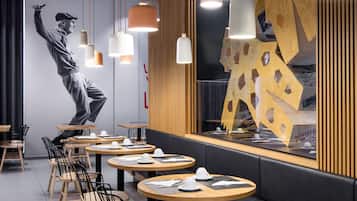 A modern restaurant interior with round tables, black chairs, and pendant lighting.