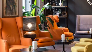 Ein modernes Wohnzimmer mit orange- und gelber Einrichtung, einem großen Fenster mit Pflanzen und einer schwarz-weißen Wand.