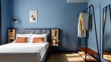 A bedroom with a bed, bedside tables, a hanging light, a wall-mounted mirror, and a clothes rack.