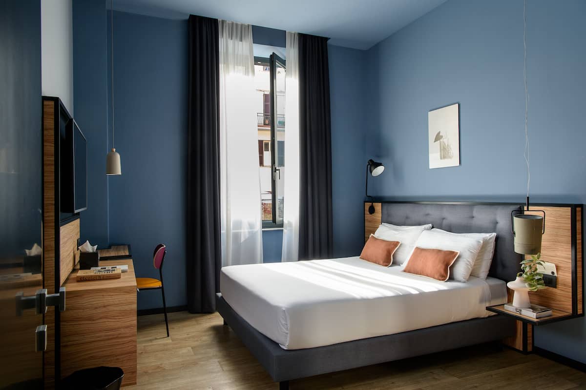 Een moderne slaapkamer met een groot bed, een bureau, een stoel en een nachtkastje met een lamp.