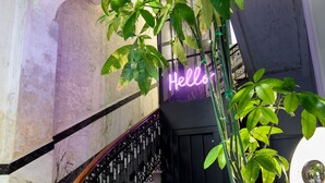 Eine Treppe mit einem neonbeleuchteten „Hello“-Schild, einem Metallgeländer und einem Blumentopf.