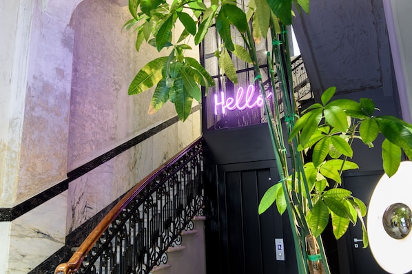 A staircase with a neon "Hello" sign, a metal railing, and a potted plant. - The Poet Hotel (La Spezia)