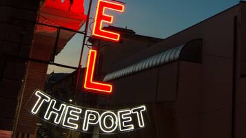 A neon sign for "HOTEL THE POET" with a classic architectural backdrop.