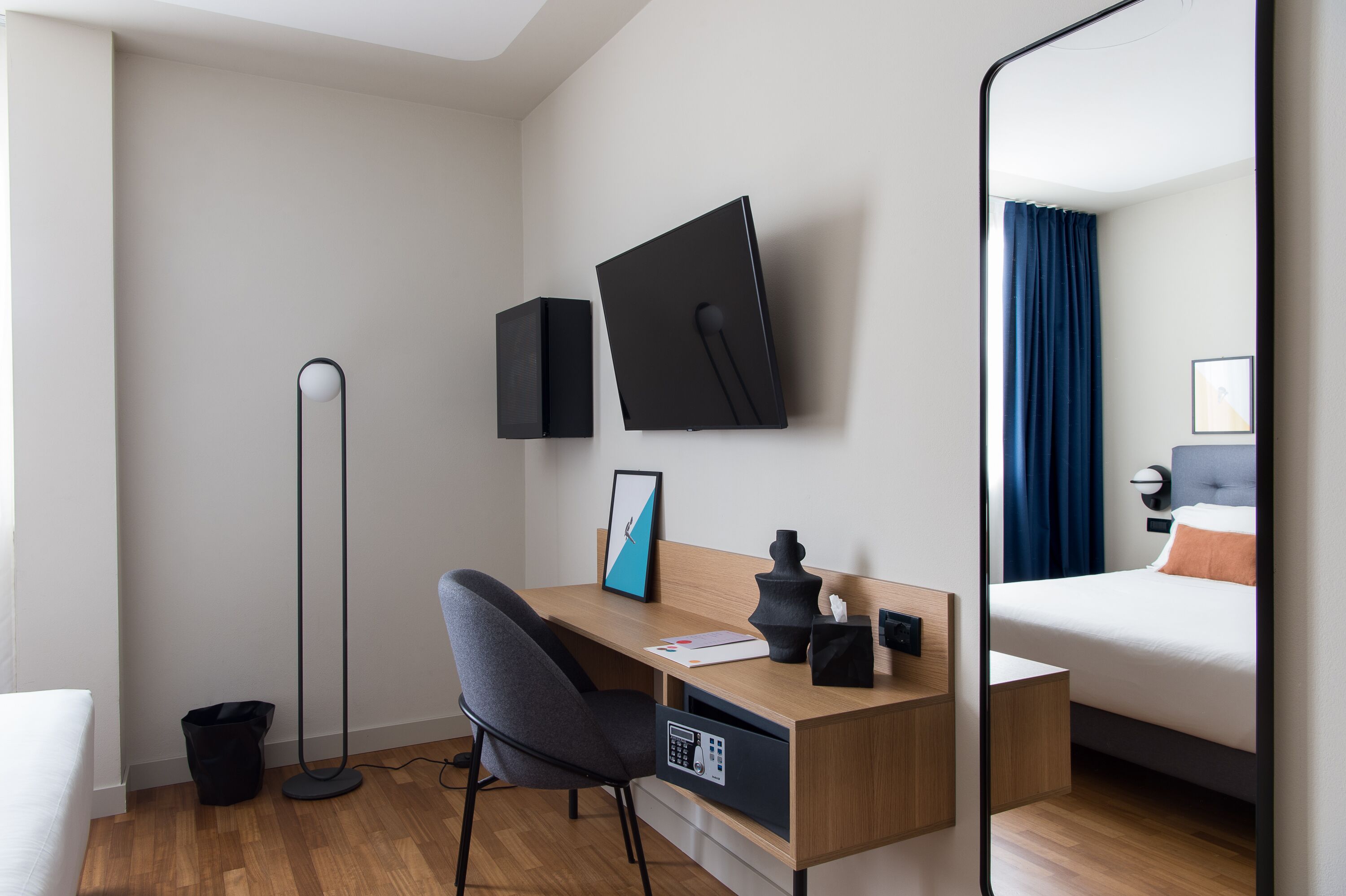 Una habitación de hotel moderna con un escritorio de madera, una silla, una cama con cortinas azules, un televisor de pantalla plana y una lámpara de pie.