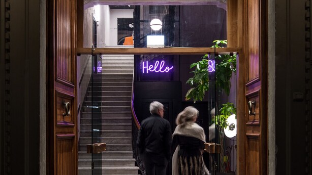 Ein Hotel Eingang mit einem Neon-Schild mit der Aufschrift 'Hello', einer Treppe und einer Glastür.