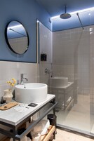 Un baño moderno con un espejo redondo grande, un lavamanos blanco y una zona de ducha con mampara de vidrio.