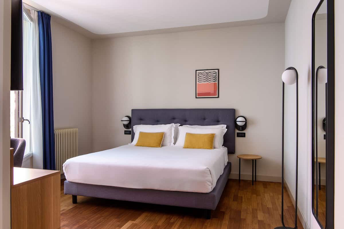 Een netjes ingerichte hotelkamer met een bed, nachtkastjes, een stoel en een kleintje tafel.