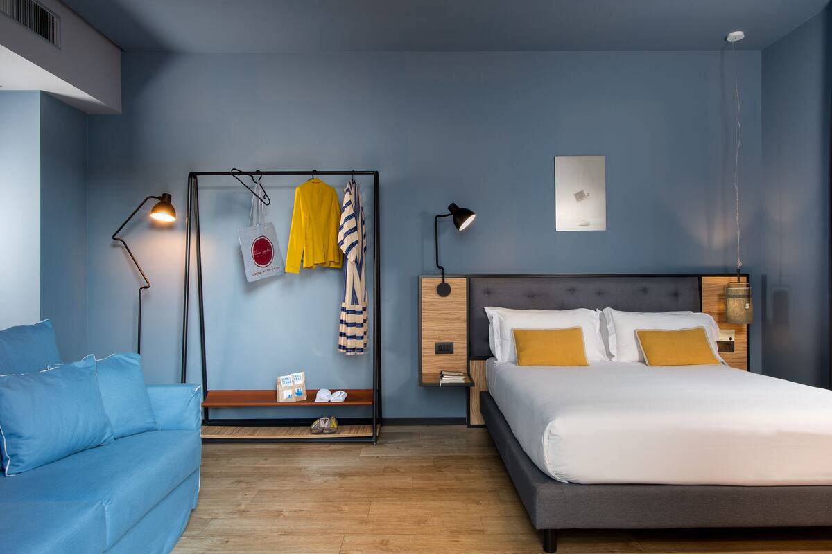 Een moderne slaapkamer met een bed, een blauwe bank, een hangende opbergkast en nachtkastjes.