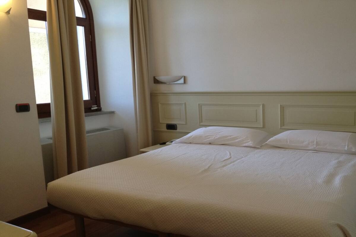 A neatly made bed with a headboard, a bedside table, and a window with curtains.