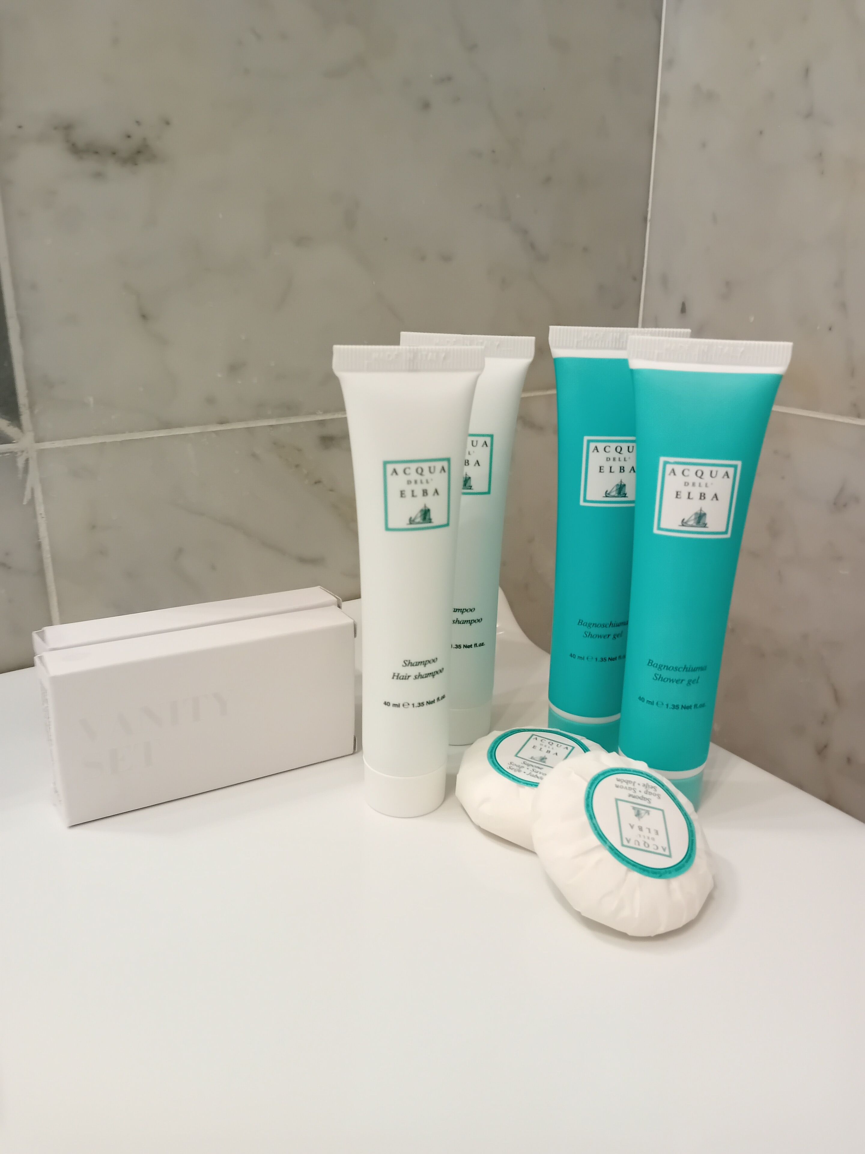 A bathroom with toiletries including a white vanity, a white box, and two bottles of Elba shower gel.