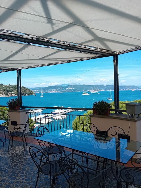A terrace with a glass table and chairs, overlooking a marina with boats and a clear blue sea. - Hotel Paradiso (Portovenere)