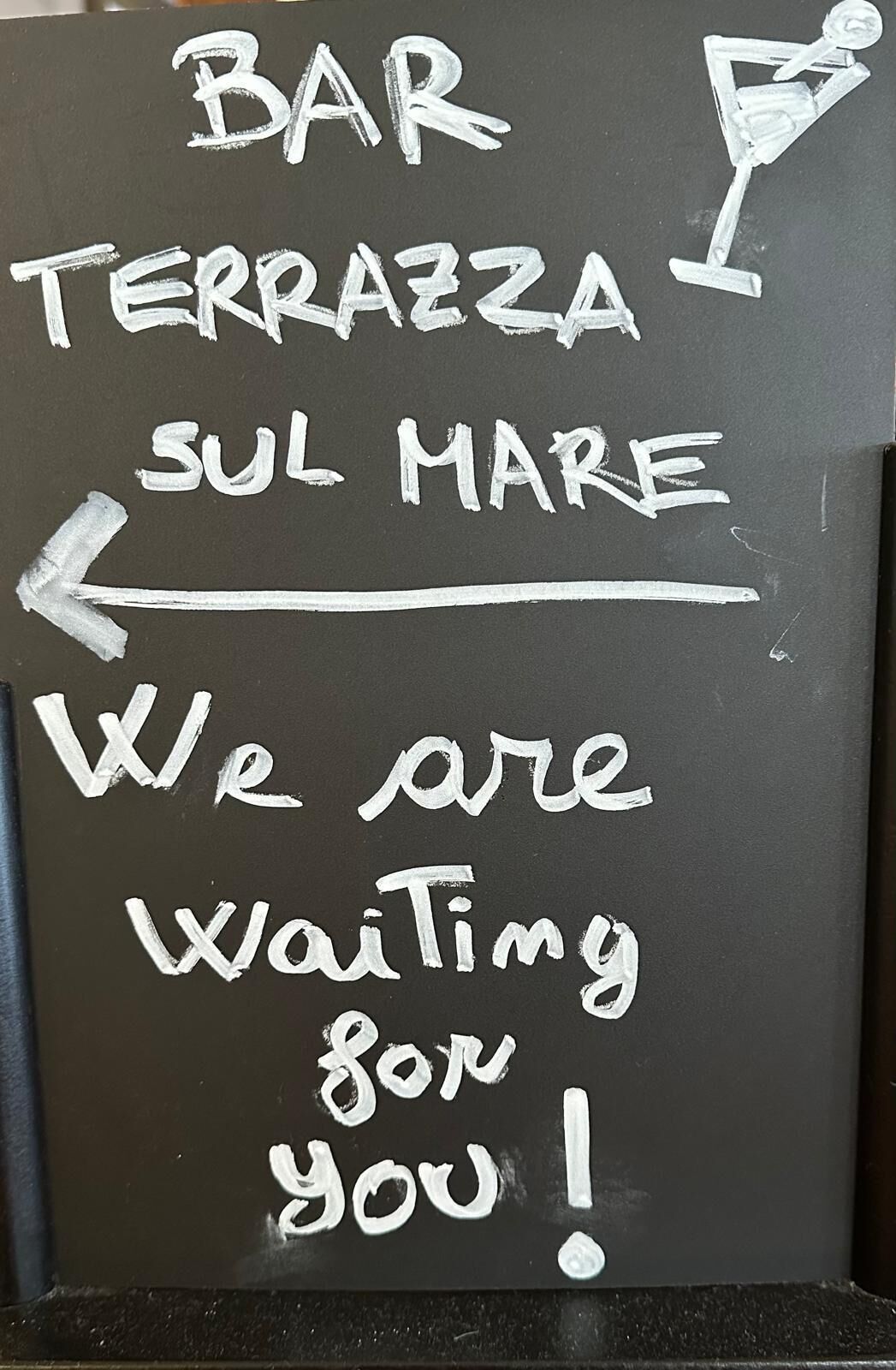 Eine Kreidetafel mit den Aufschriften 'BAR', 'TERRAZZA', 'SUL MARE' und 'Wir warten auf Sie!'