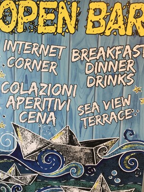 Un letrero con la inscripción 'OPEN BAR', 'INTERNET CORNER', 'BREAKFAST DINNER DRINKS', 'COLAZIONI', 'APERITIVI', 'SEA VIEW' y 'TERRACE'.