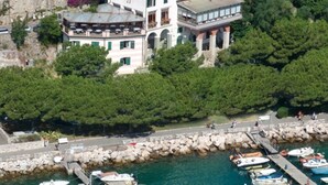 A multi-story building with a balcony, located near a rocky waterfront with boats docked. - Hotel Paradiso (Portovenere)