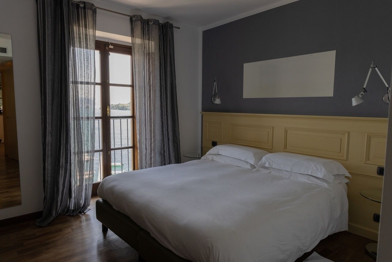 A bedroom with a bed, a window with curtains, a bedside lamp, and a view of the outdoors.