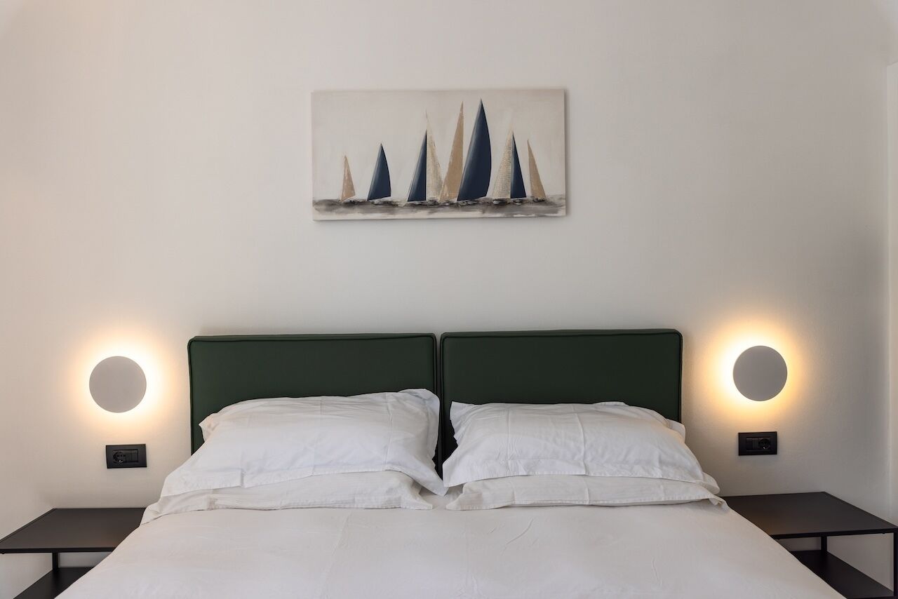 A bedroom with a bed, two bedside tables, and a wall-mounted painting of sailboats.