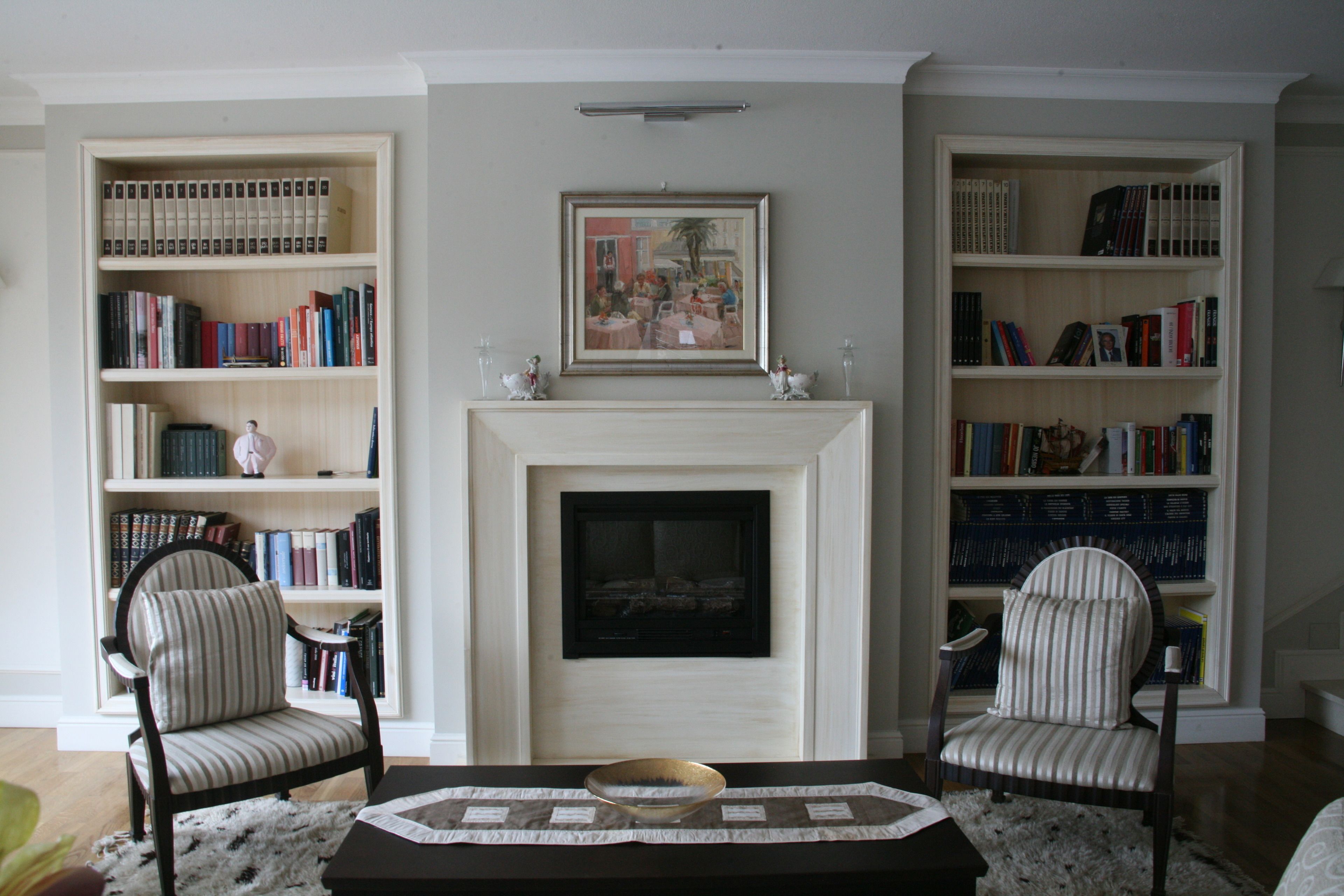 Ein Wohnzimmer mit Kamin, zwei Sesseln, einem Couchtisch und zwei Bücherregalen voller Bücher.