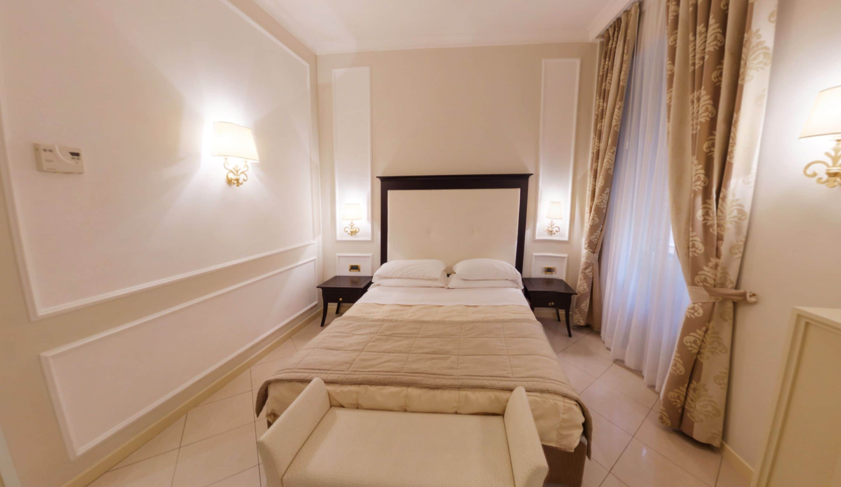 A hotel room with a large bed, two bedside tables, a nightstand, a chair, and a window with curtains.