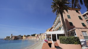 A beachfront hotel with a terrace, palm trees, and a clear blue sky.