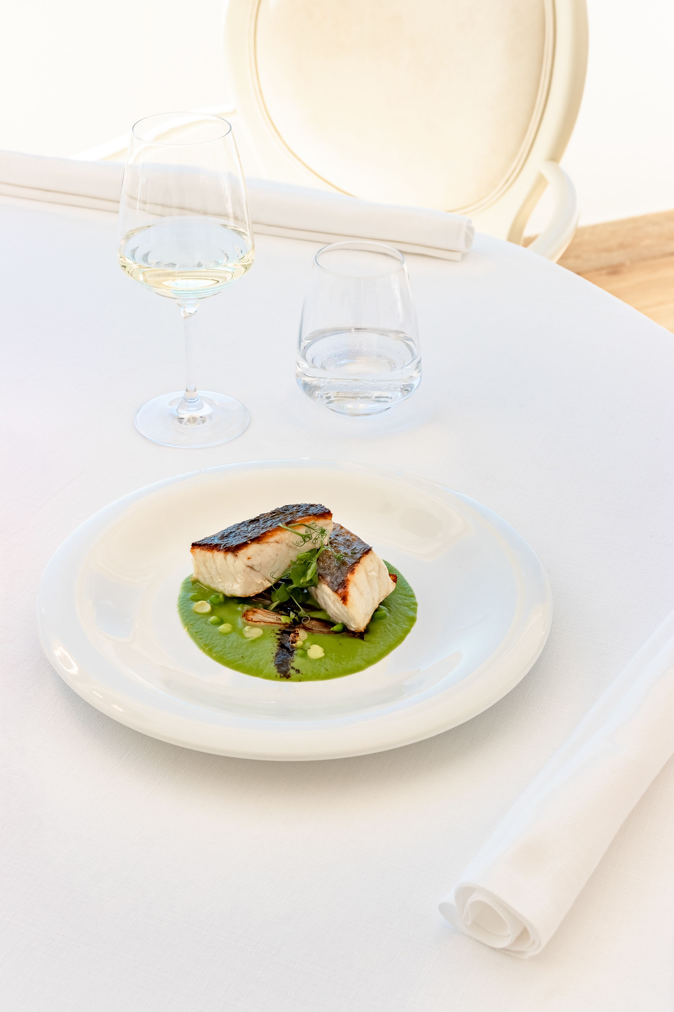 Une table à manger blanche, avec une assiette blanche contenant de la nourriture, deux verres à vin vides et une serviette blanche.