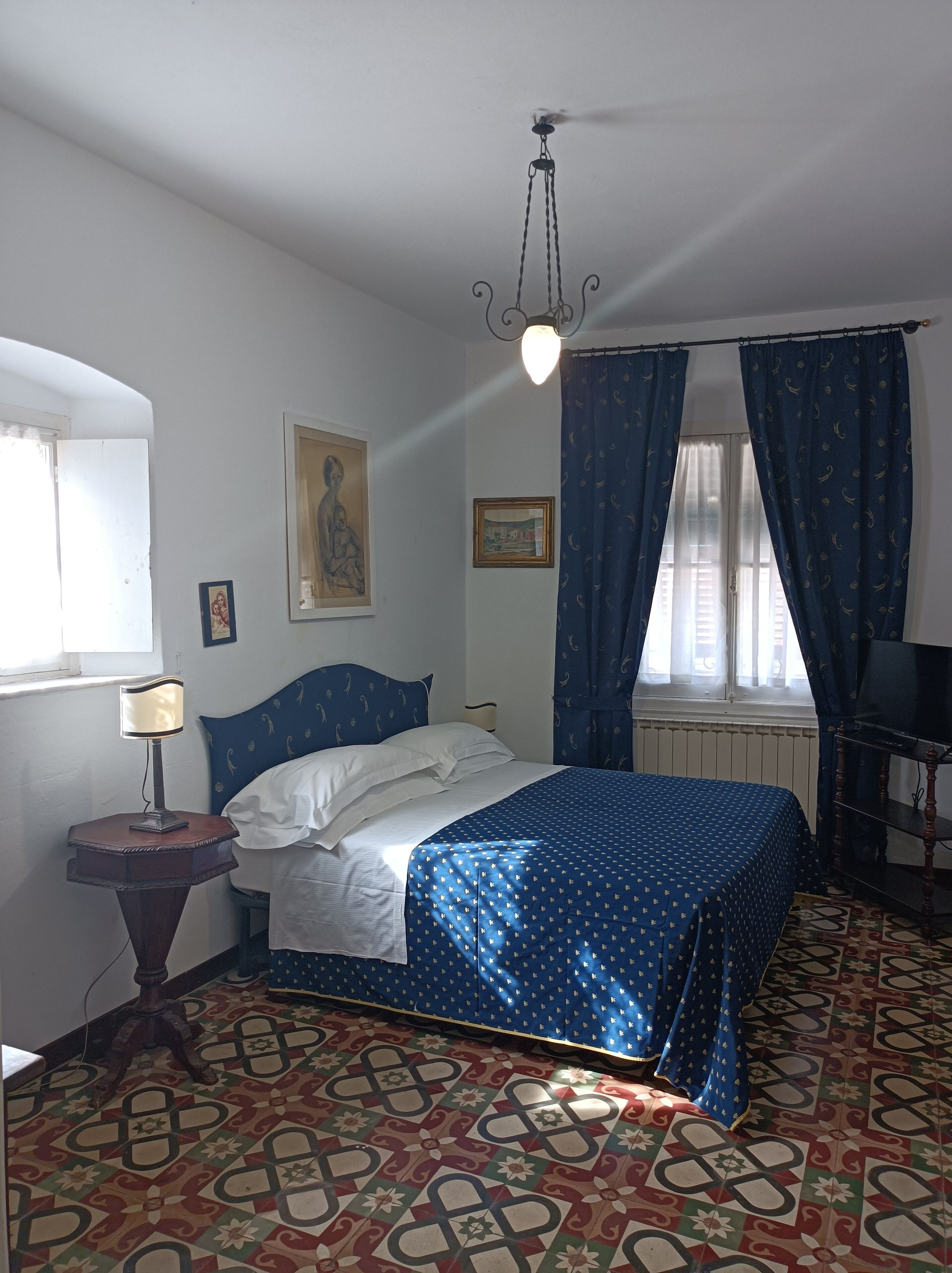 A bedroom with a bed, a nightstand, a lamp, a ceiling fan, and patterned curtains.