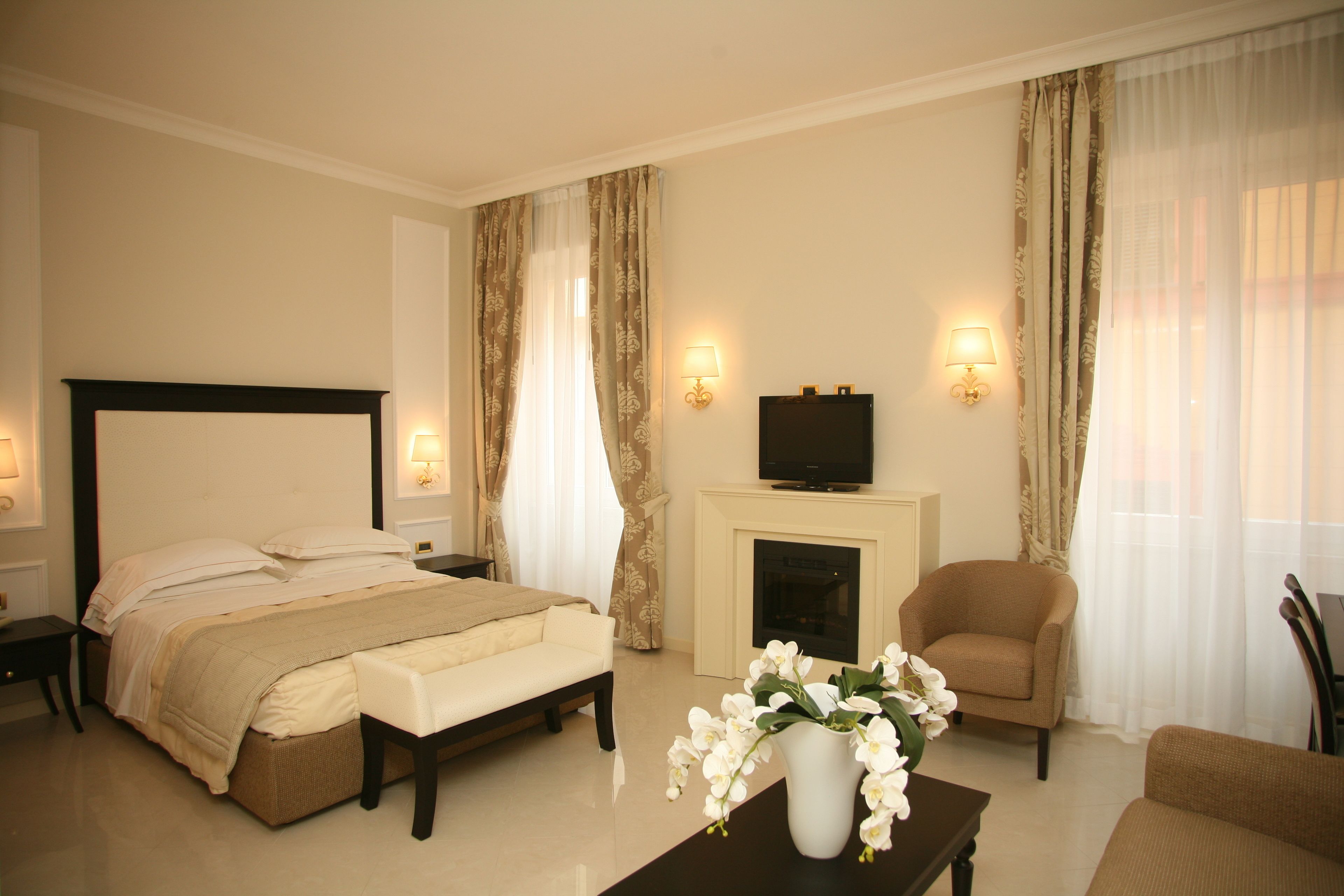 Een hotelkamer met een bed, een slaapbank, een televisie, een open haard en een bloemenvaas.