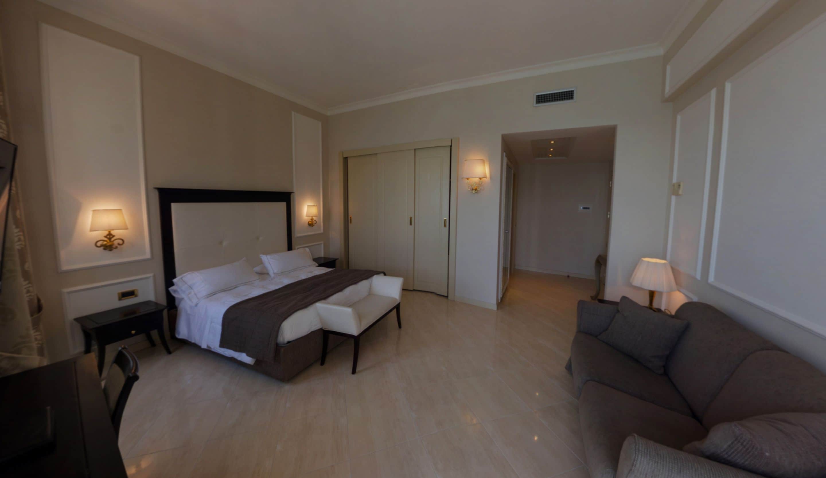 Habitación de hotel con cama, mesitas de noche, escritorio, silla, sofá y lámpara.