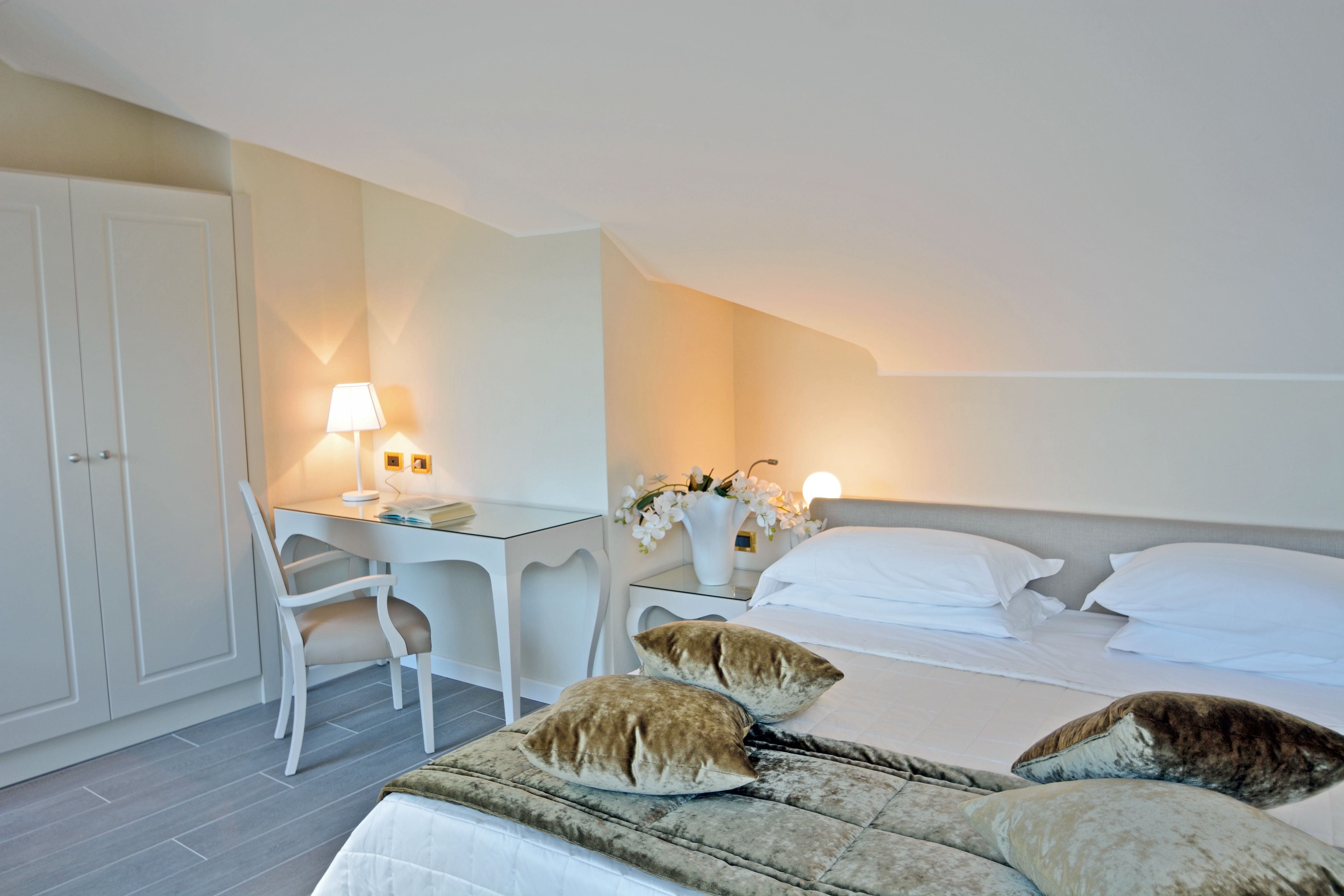 Una camera da letto con un letto, due cuscini, un comodino con una lampada, una sedia e una scrivania.