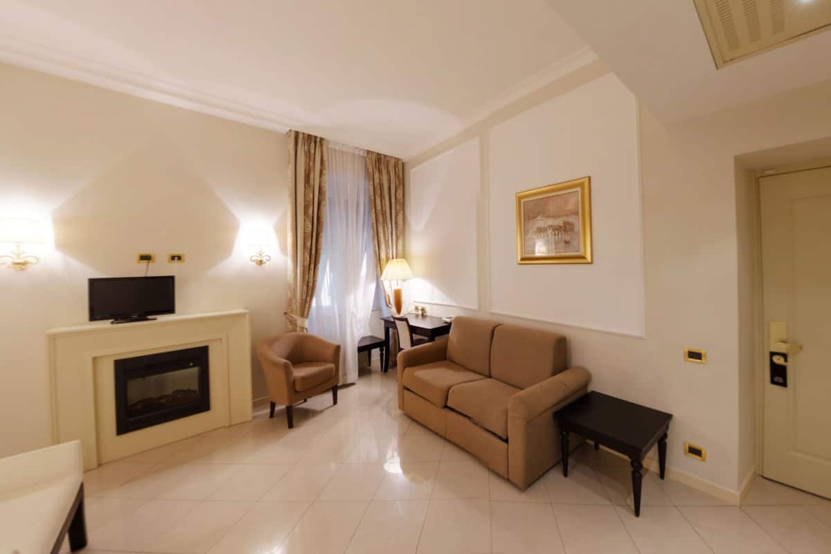 Een hotelkamer met een bank, fauteuil, televisie, open haard en een schilderij aan de muur.
