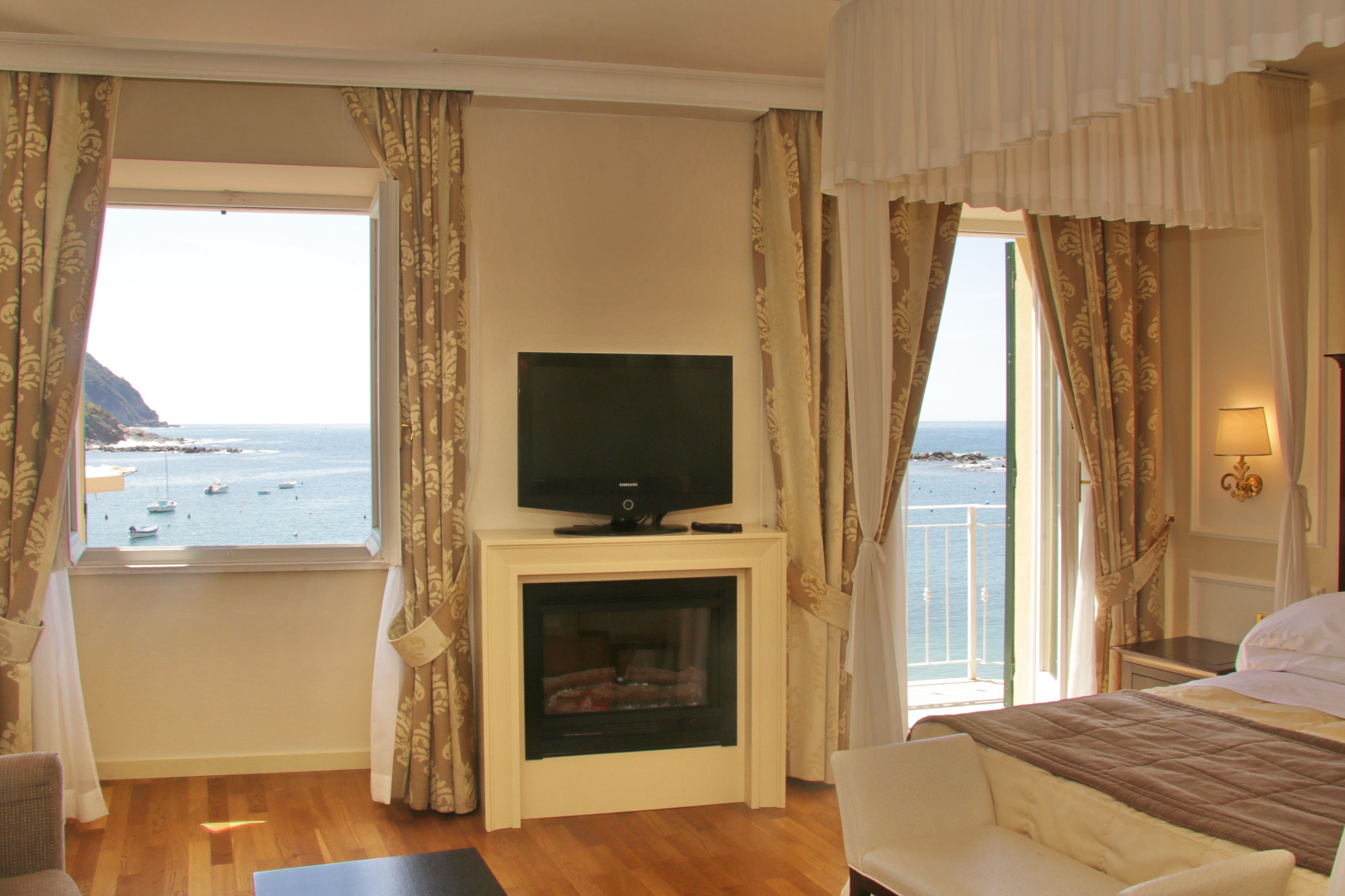 Een hotelkamer met een televisie op een standaard, een open haard, een bed en uitzicht op zee.