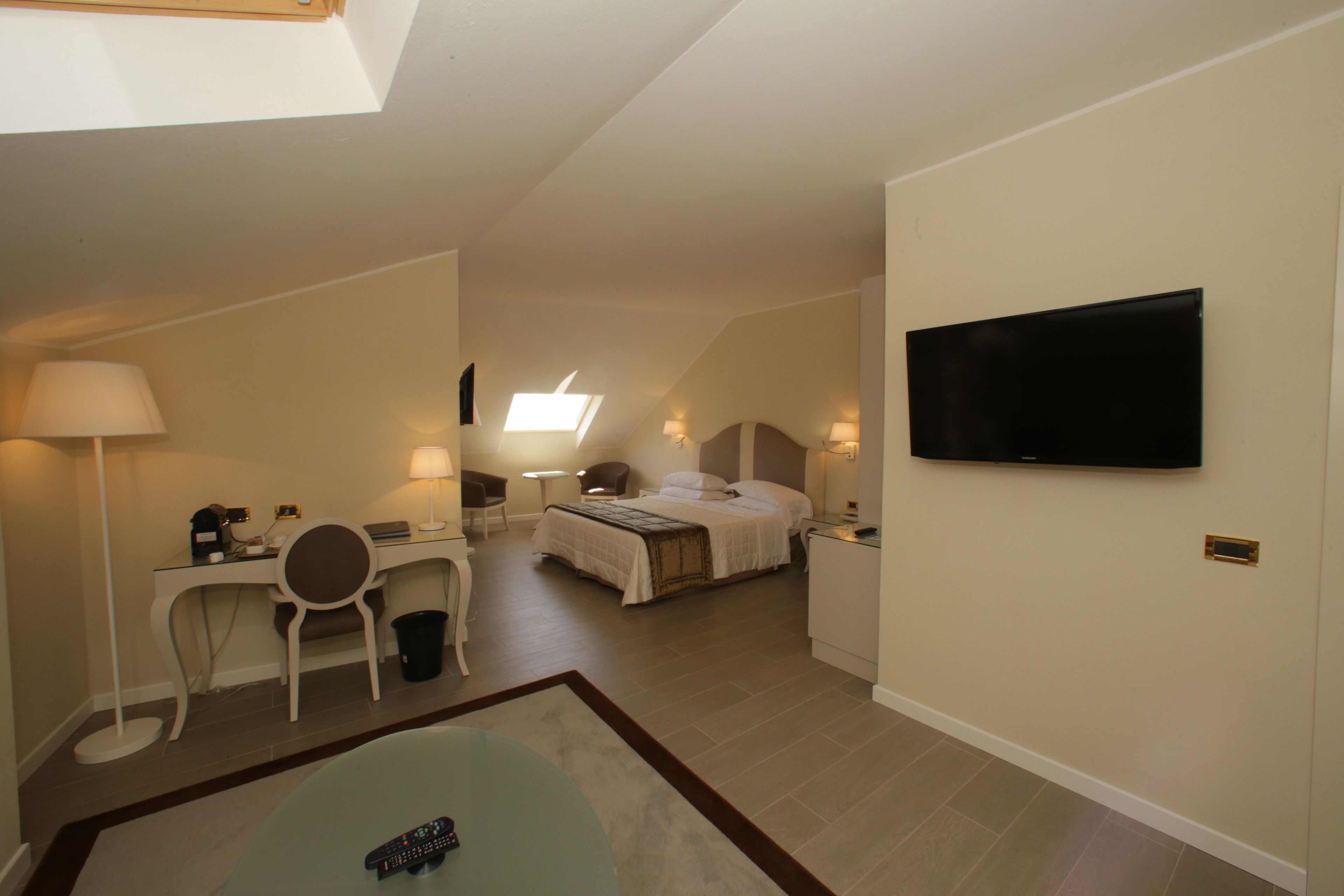 Ein kleines Hotelzimmer mit Bett, Schreibtisch, Stuhl und einem an der Wand befestigten Fernseher.