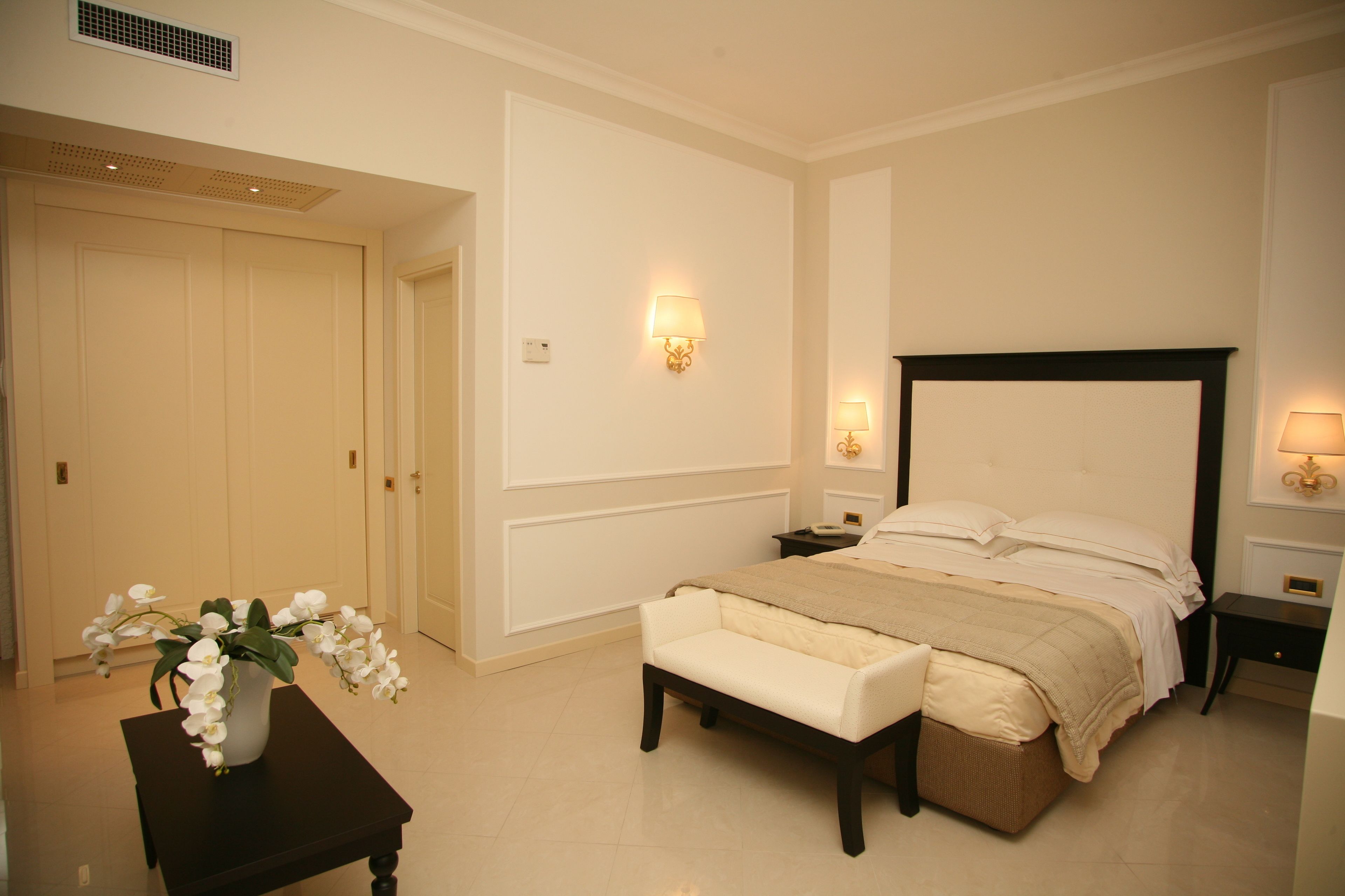 A bedroom with a bed, bedside tables, a bench, and a vase of flowers.