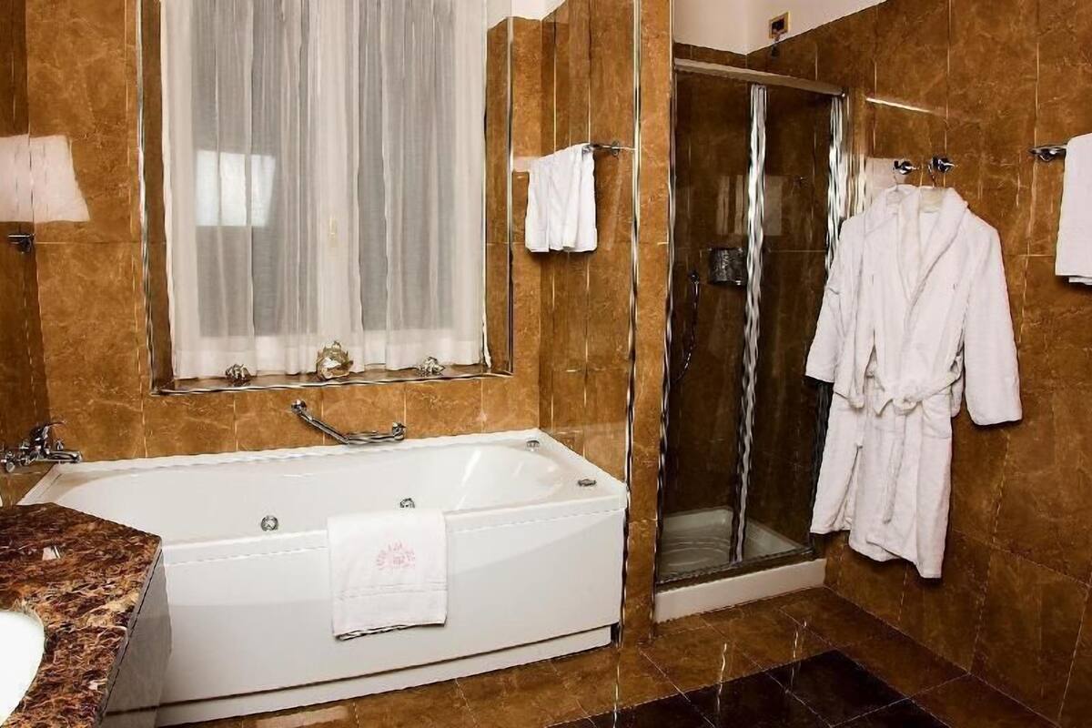 Een badkamer met een bad, een douche met glazen wanden en een badjas hangend aan de muur.