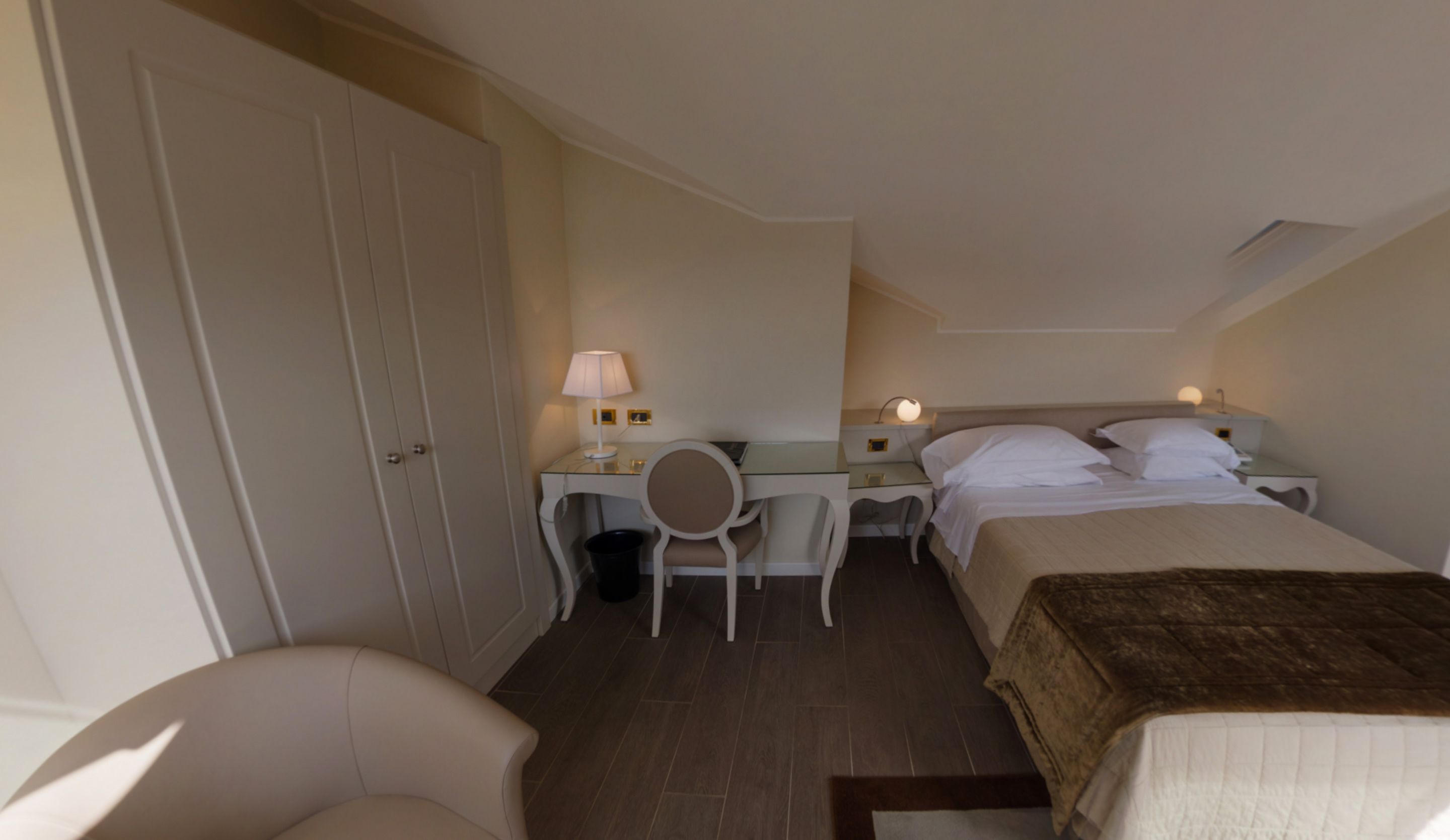 Una camera d'albergo con un letto, una scrivania con una sedia, una lampada e un armadio.