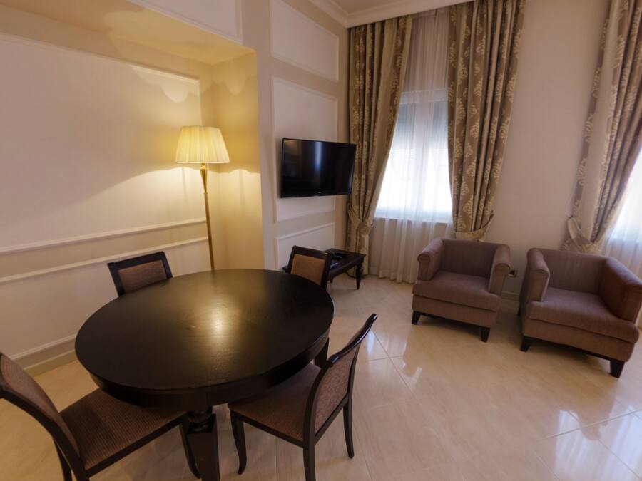 A modern living room with a round dining table, two armchairs, a sofa, a flat-screen TV, and a lamp.