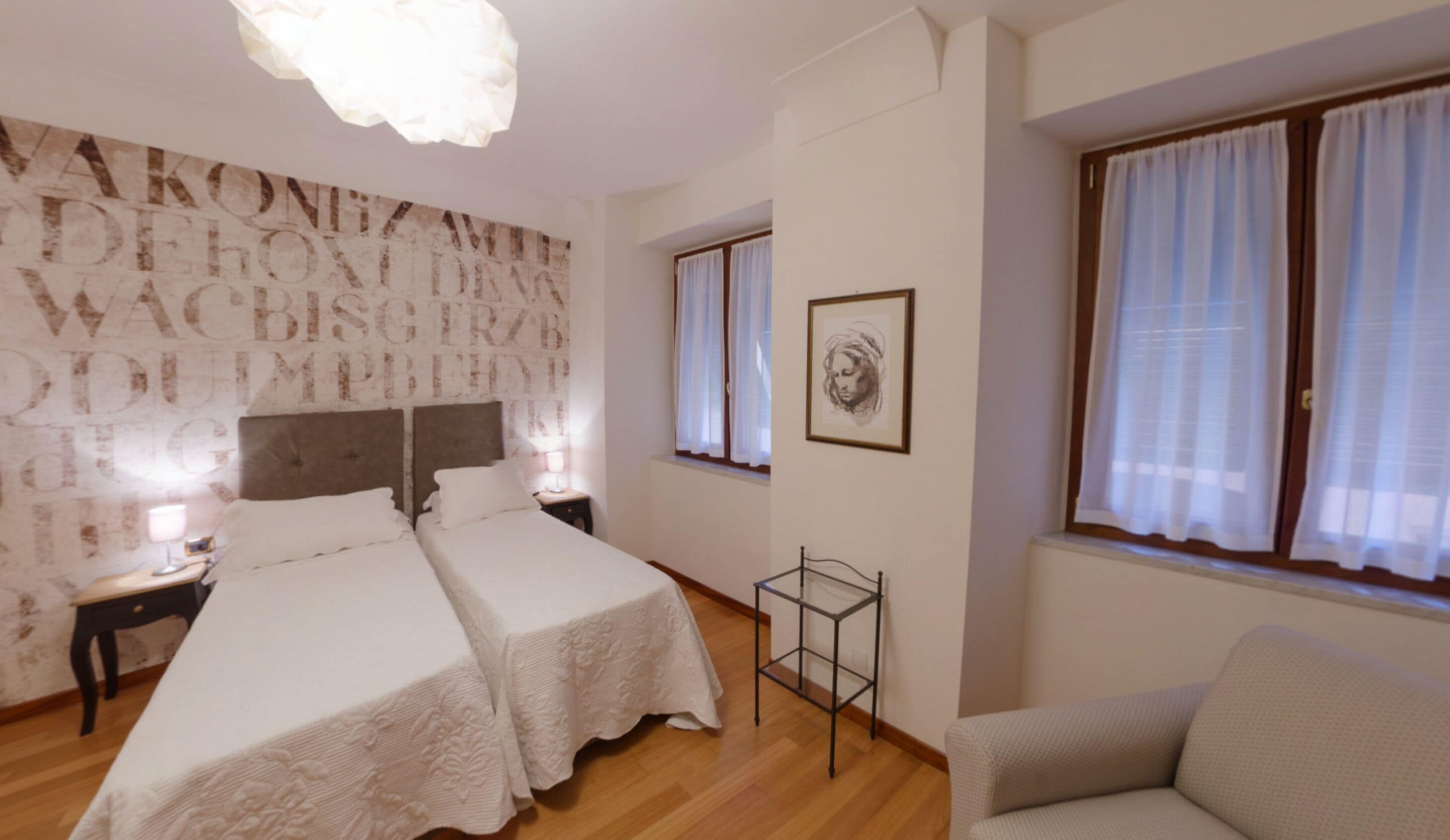 Ein Hotelzimmer mit zwei Betten, einem kleinen Tisch, einem Stuhl und einem Fenster mit Vorhängen.