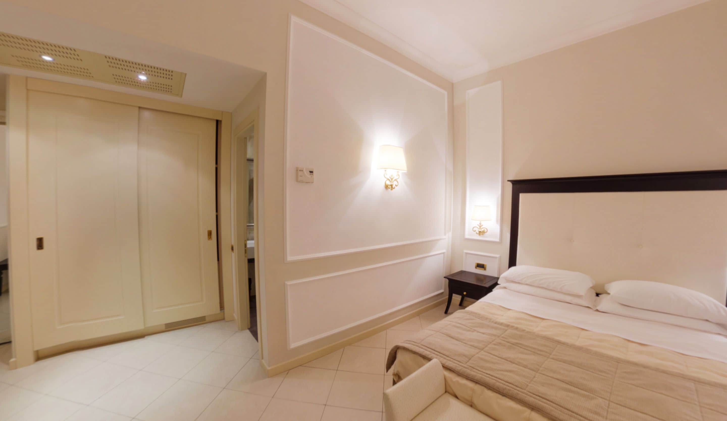 Una habitación de hotel con cama, mesita de noche, lámpara de pared y armario.