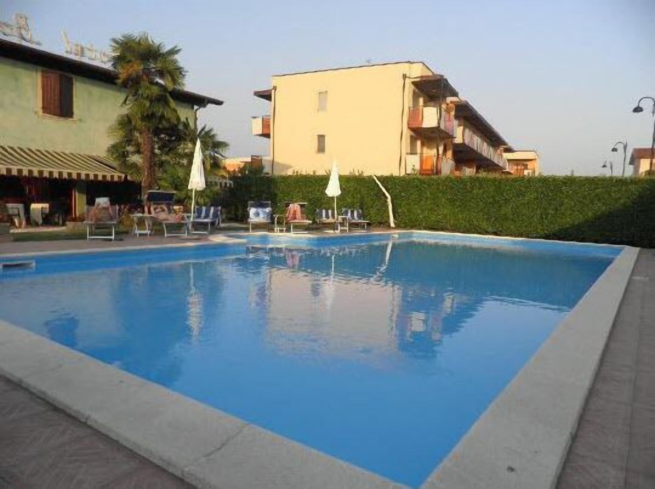 A swimming pool with lounge chairs and umbrellas, surrounded by greenery and buildings.
