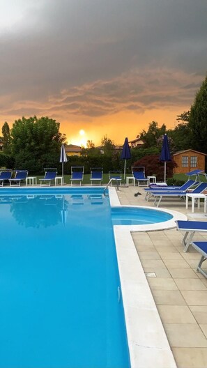A swimming pool with lounge chairs and umbrellas, surrounded by trees and a building in the background. - Bolero (Sirmione)