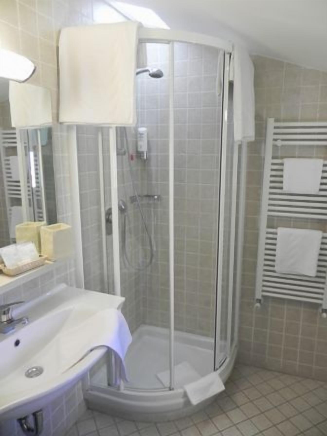 A corner bathroom with a glass-enclosed shower, a sink with a mirror, and a towel rack.