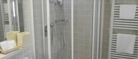 A corner bathroom with a glass-enclosed shower, a sink with a mirror, and a towel rack.