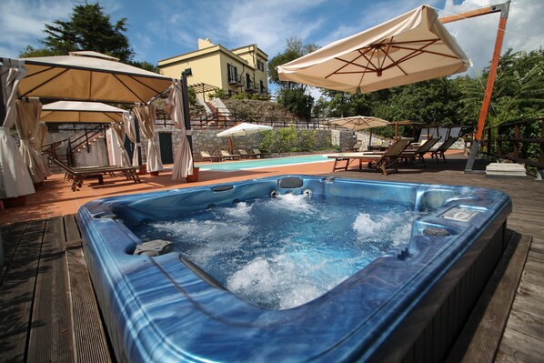 A hot tub with a wooden deck, lounge chairs, and umbrellas. - Relais San Rocco (Casarza Ligure)