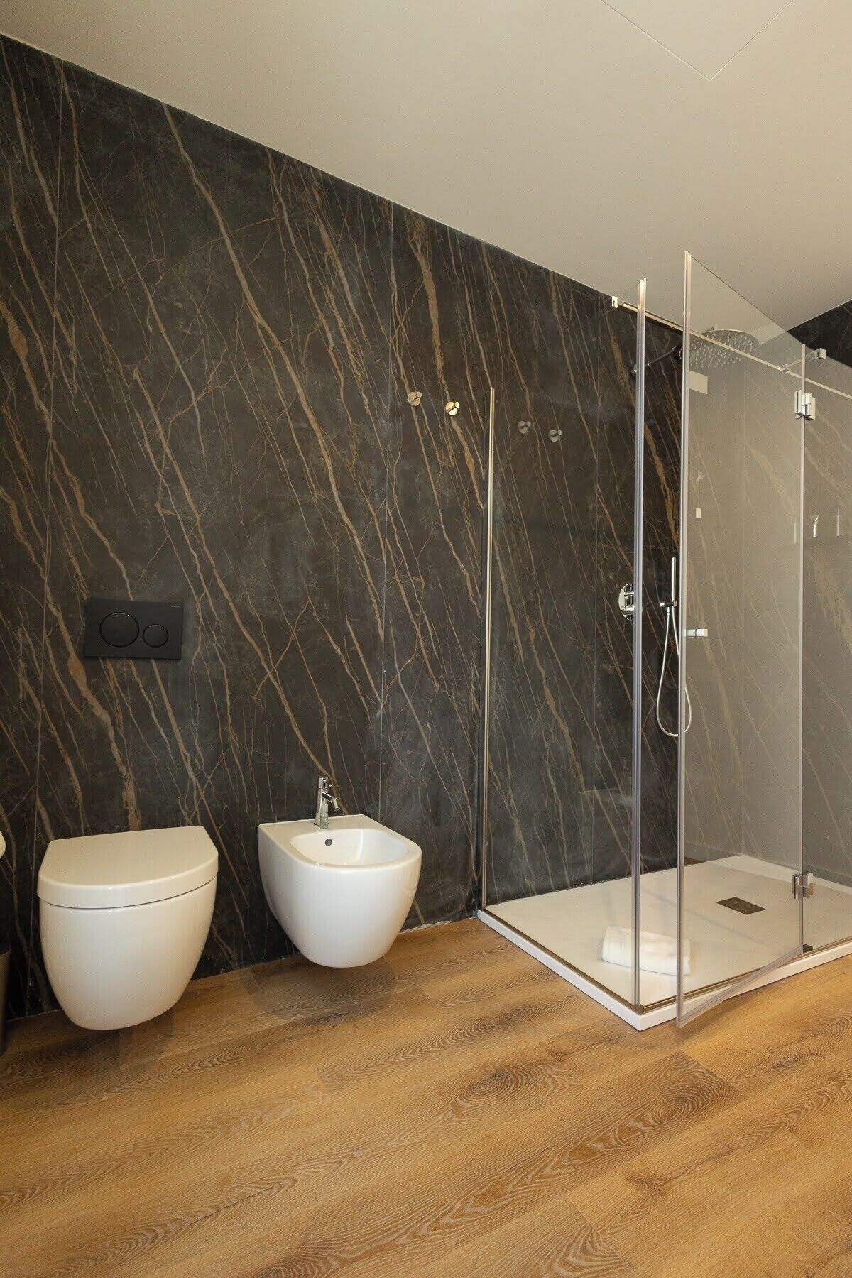 A modern bathroom with a marble wall, a toilet, a bidet, and a glass-enclosed shower.